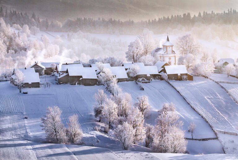 Sat de iarnă acoperit cu zăpadă și biserică.