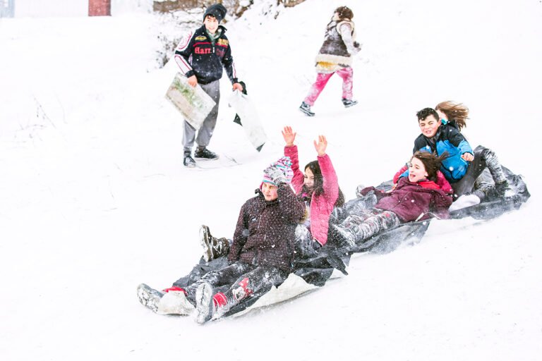 Copii se dau cu sania pe zăpadă.