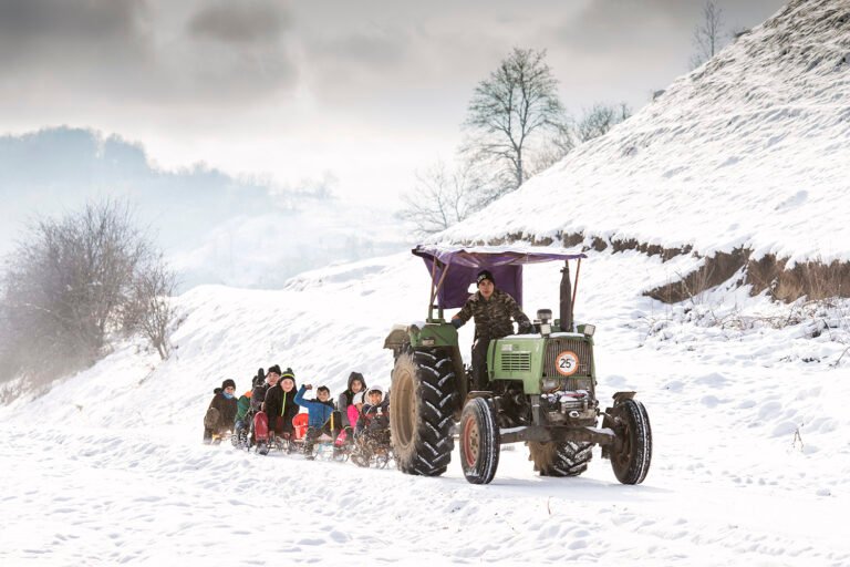 Tractor trage sănii cu copii pe zăpadă.