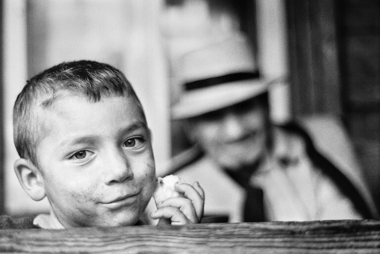 Băiat zâmbitor lângă om în pălărie.