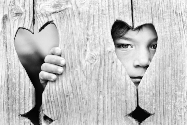 Copil priveste prin gard cu forma de inima.