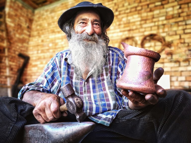 Fierar bătrân ținând ciocan și vas de cupru.