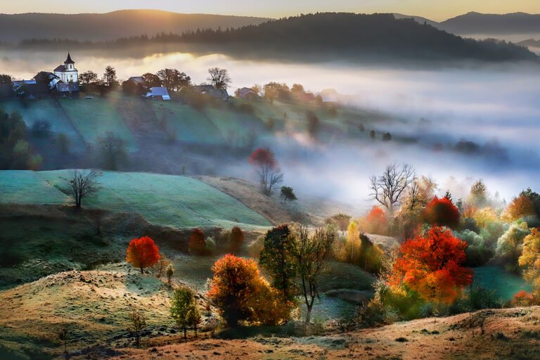 Peisaj rural cu ceață și copaci colorați toamna.