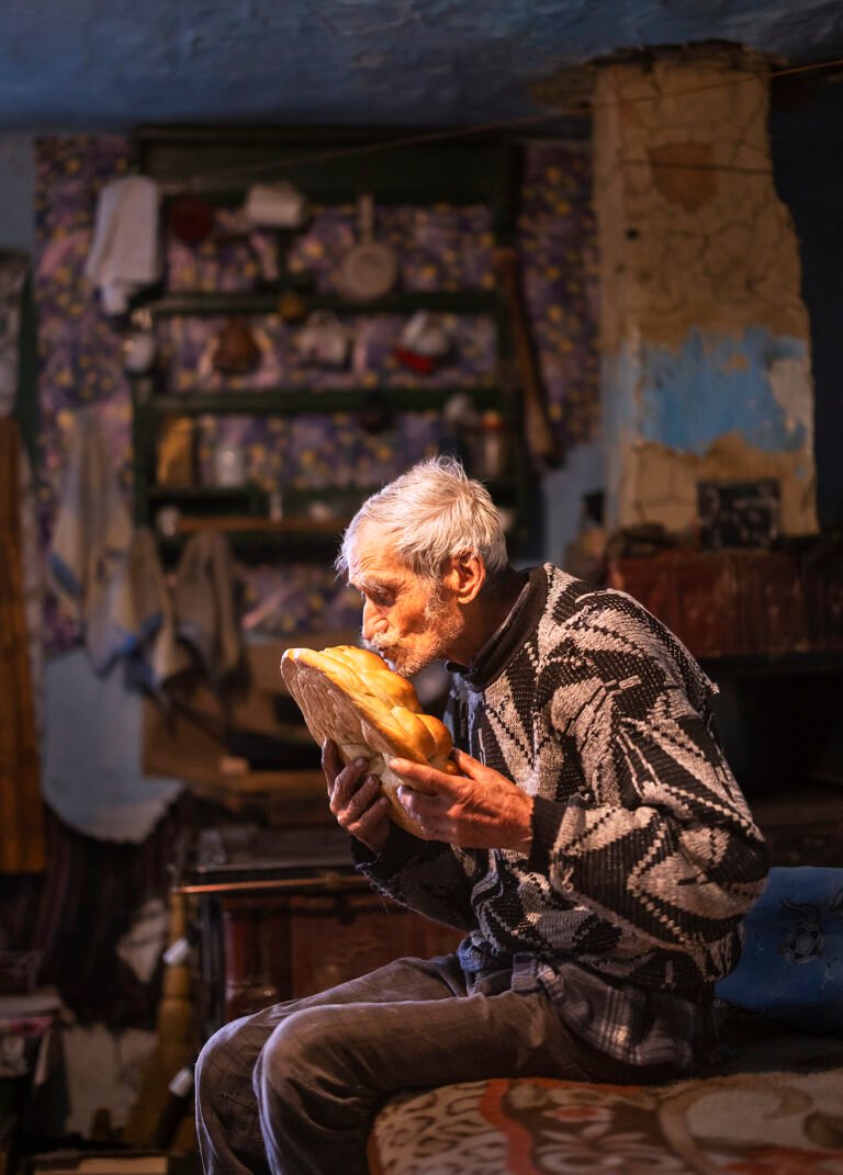Bătrân sărutând pâinea în casă tradițională.