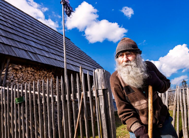 Bătrân cu barbă lungă lângă gard rustic