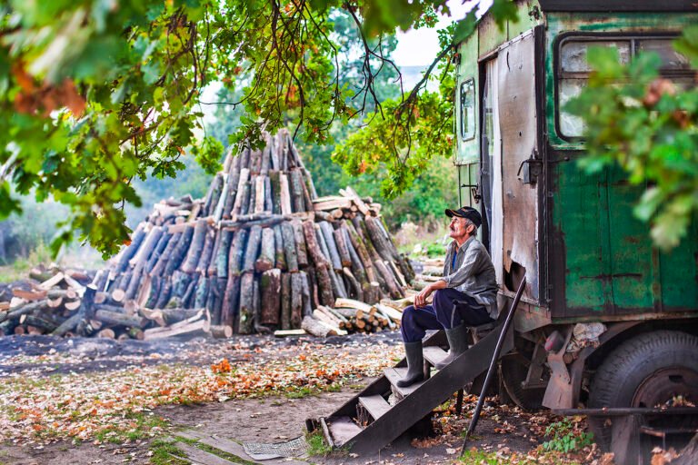 Bătrân odihnindu-se lângă camion și grămadă de lemne.