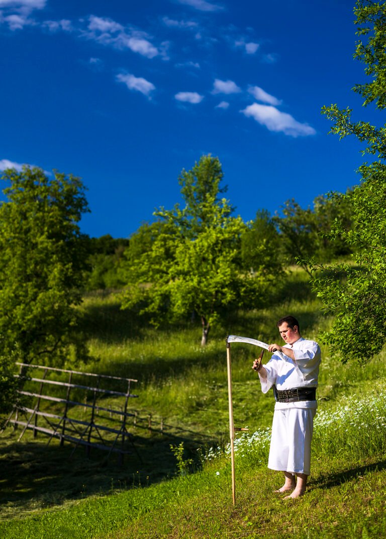 Bărbat în port popular ascute o coasă.