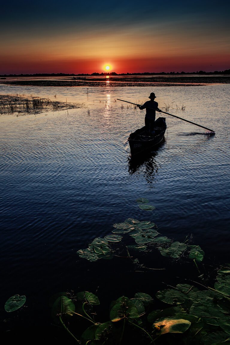 Pescar în barcă pe lac la apus.