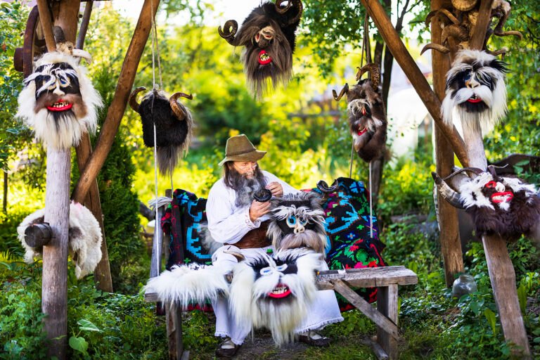 Bărbat meșterind măști tradiționale în grădină cu verdeață.