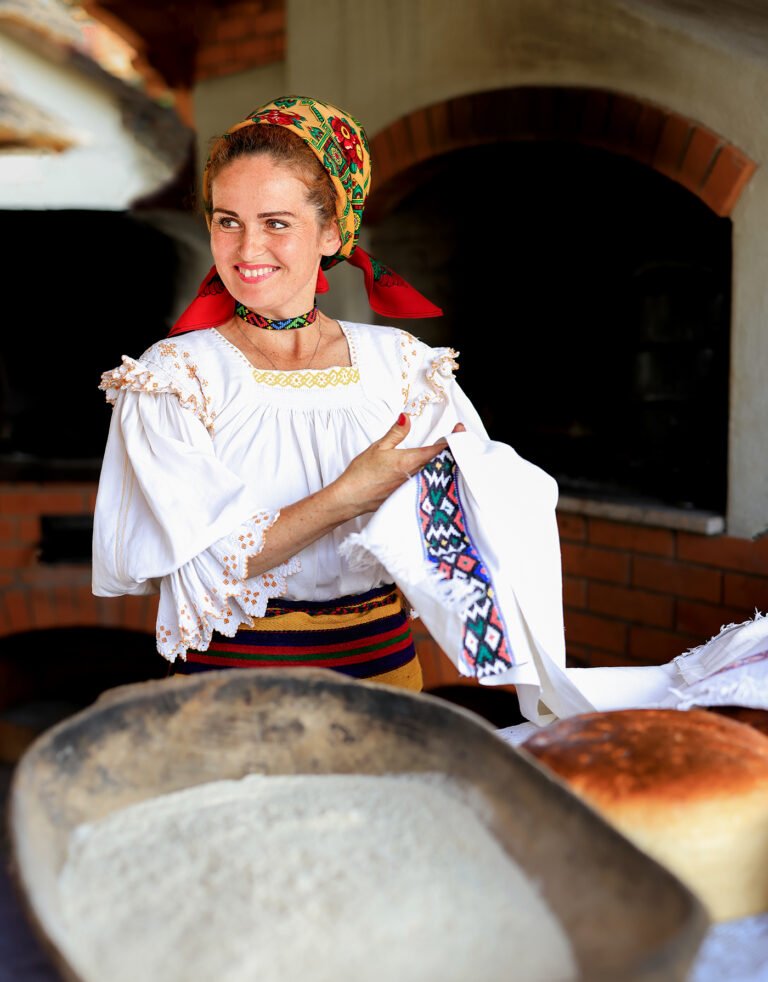 Femeie în costum tradițional lângă cuptor de pâine.