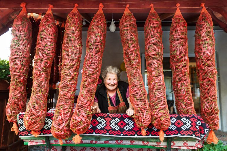 Femeie vânzătoare zâmbind printre ardei uscați atârnați.