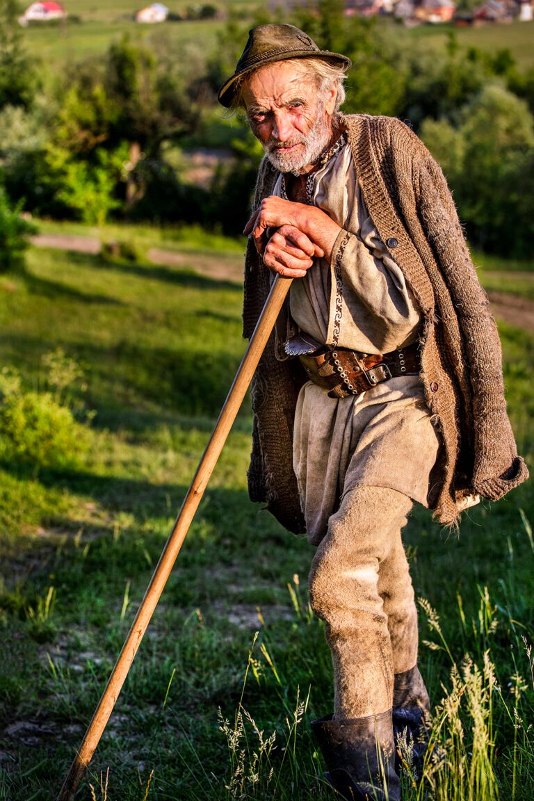 Bătrân sprijinindu-se de un baston în natură