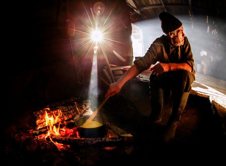 Om gătește la foc în șură rustică.