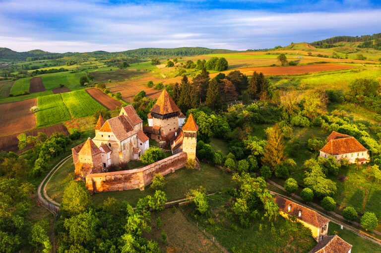 Biserică fortificată rurală în peisaj de dealuri verzi.