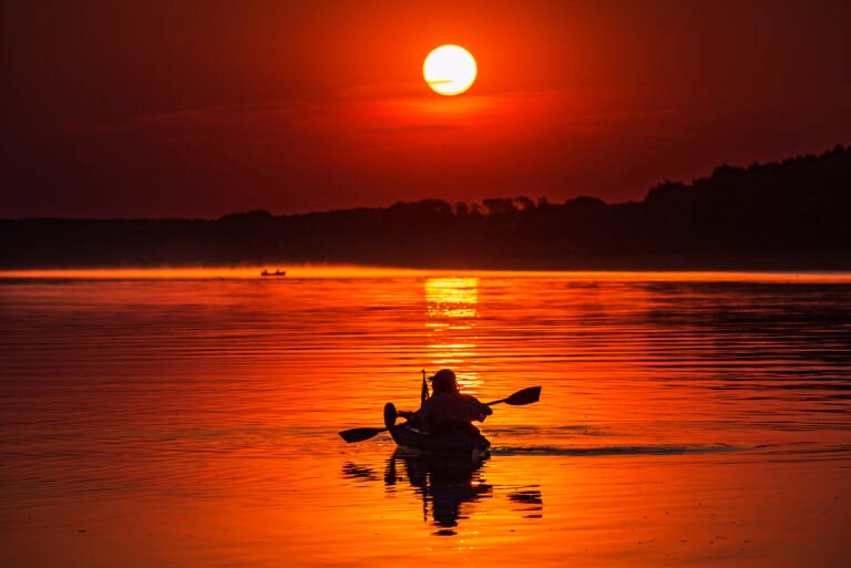Caiacist la apus pe un lac liniștit.
